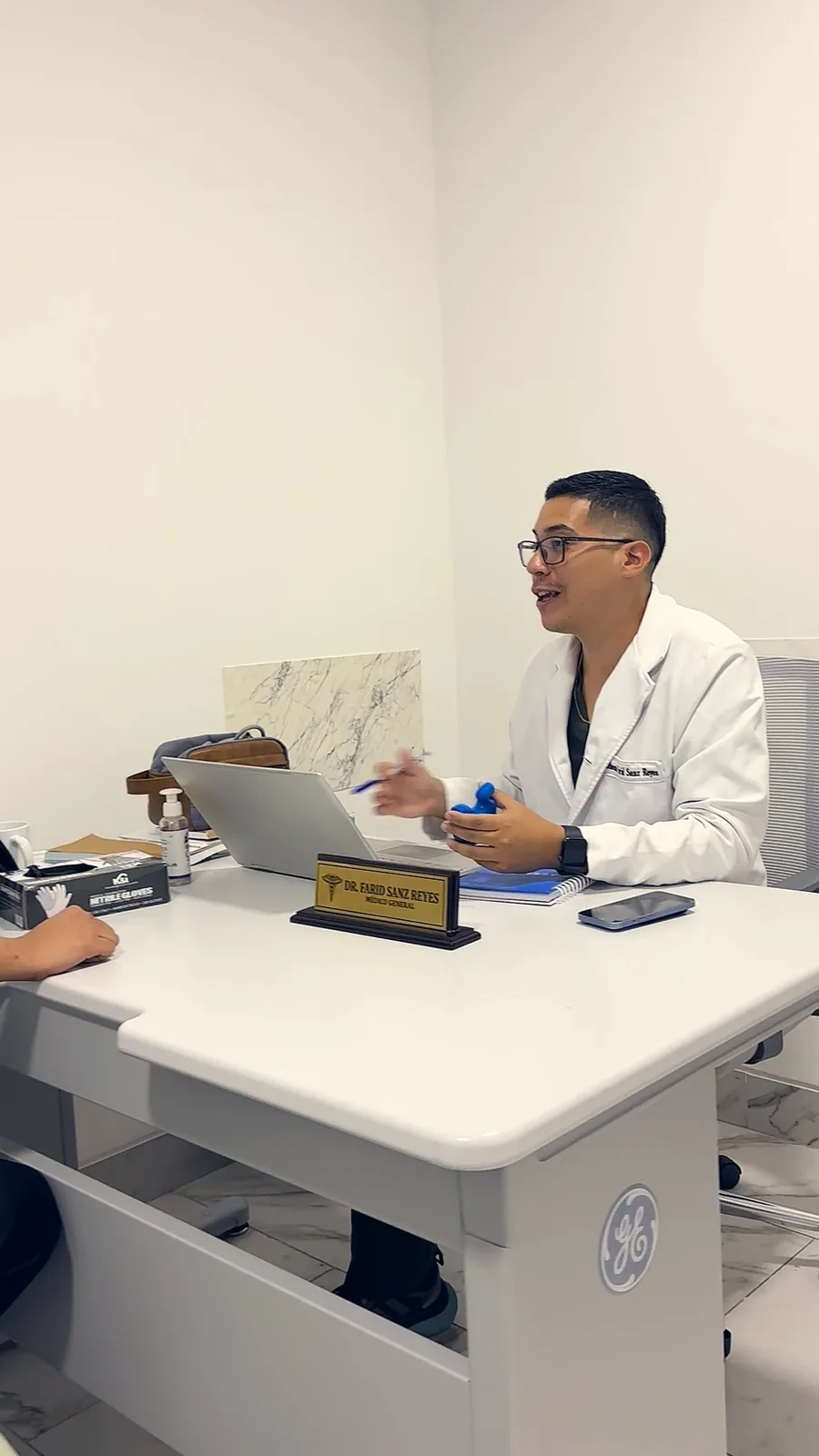 Consulta presencial en el consultorio del Dr. Farid Sanz, con su placa de médico general sobre el escritorio.