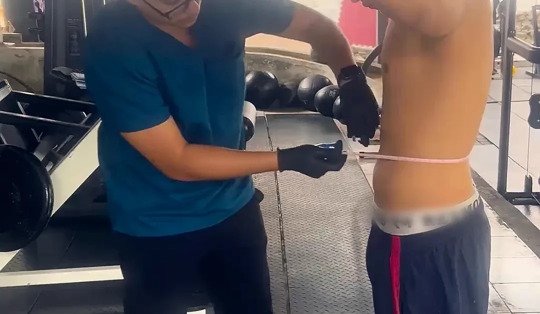 El doctor mide la cintura de un deportista en el gimnasio.